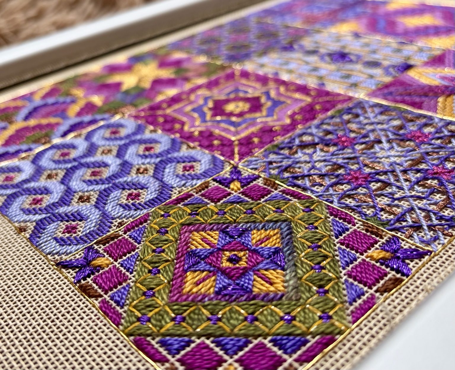 Close-up of The Bazaar Collection showing raised counted-canvas stitches, metallic gold outlining, and layered purple, pink, green, and brown threads.